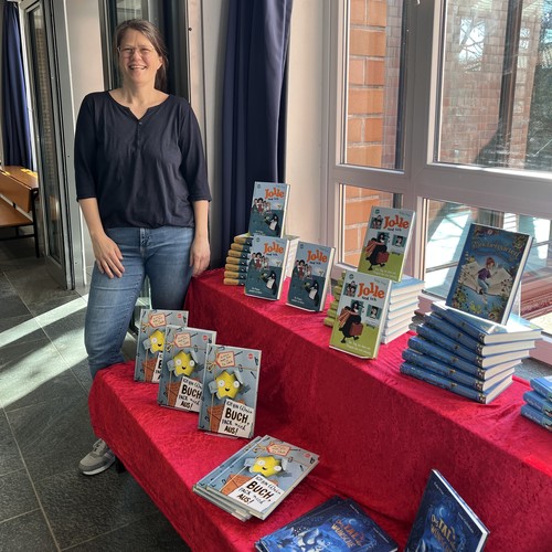 Das Foto zeigt die Autorin Katja Frixe vor ihren Büchern.