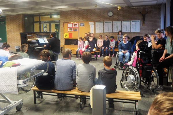 Ein Foto zeigt den Pianisten Adrian Morreale und einige Schüler:innen der Brückenschule beim gemeinsamen Singen von Adventsliedern.