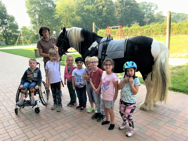 Ein Foto zeigt das Pferd "Wesley" mit einigen Schüler:innen und Frau Deitert, der Besitzerin des Pferdes.