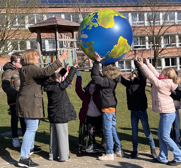 Das Bild zeigt  Brückenschüler:innen beim Spiel mit dem großen Erdball.