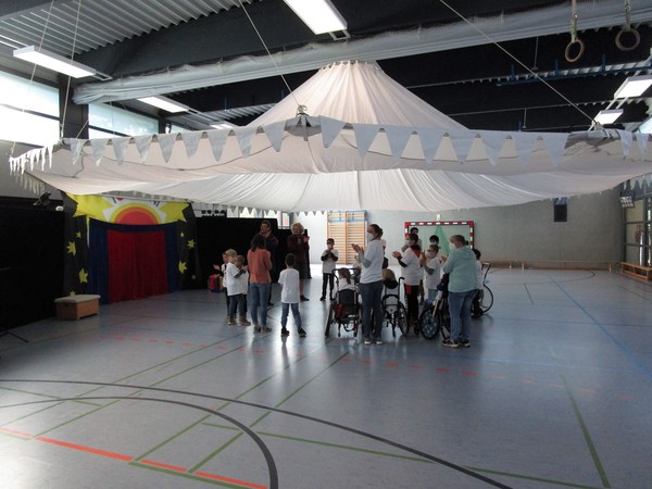 Das Foto zeigt die Turnhalle der Brückenschule mit einer Gruppe von Artisten unter dem Zirkuszelt.