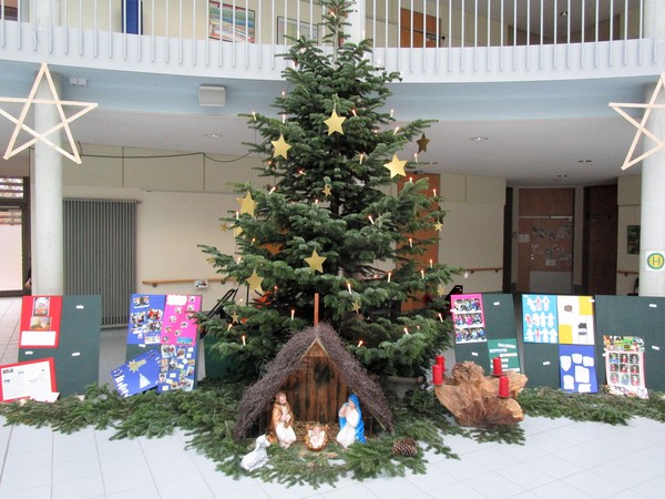 Ein Foto zeigt den geschmückten Weihnachtsbaum und die Krippe im Forum der Brückenschule.