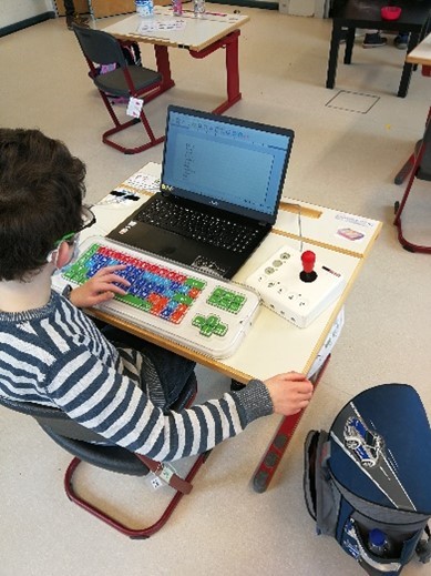 Ein Foto zeigt Leon. Er arbeitet an seinem Laptop mithilfe einer Clevy-Tastatur und eines Joysticks