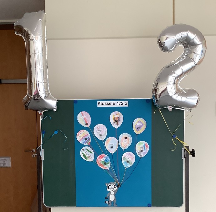 Das Foto zeigt die Tafel mit den Namen der Einschulungskindern und den Zahlenluftballons der Klasse E 1 2.