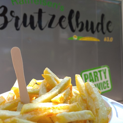 Das Bild zeigt eine Schale mit Pommes. Im Hintergrund ist ein Imbisswagen zu sehen.
