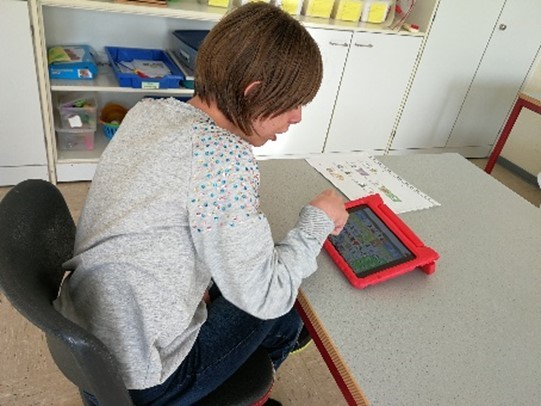 Ein Foto zeigt Johanna. Sie nutzt ein Ipad mit symbolbasiertem Wortschatzprogramm