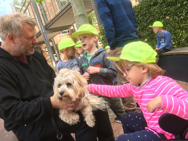 Ein Bild zeigt die Schulhündin Frieda, die auf dem Pausenhof von Schüler:innen umringt und gestreichelt wird.