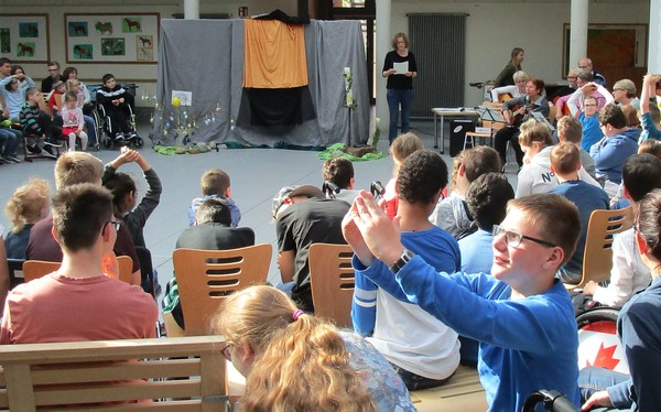 Ein Foto zeigt das mit Brückenschüler:innen und Mitarbeiter:innen gut gefüllte Forum beim Ostergottesdienst.